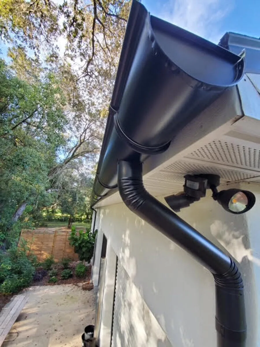 Black half-round seamless gutter with round downspout installed on a Florida home